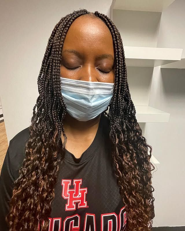 Person with braided hair wearing a blue mask and black UH hoodie, eyes closed, indoors.