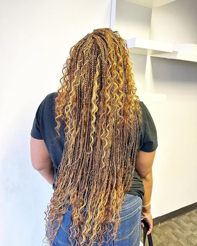 Person with long curly blonde hair standing in a hallway, seen from behind, wearing a dark shirt and jeans