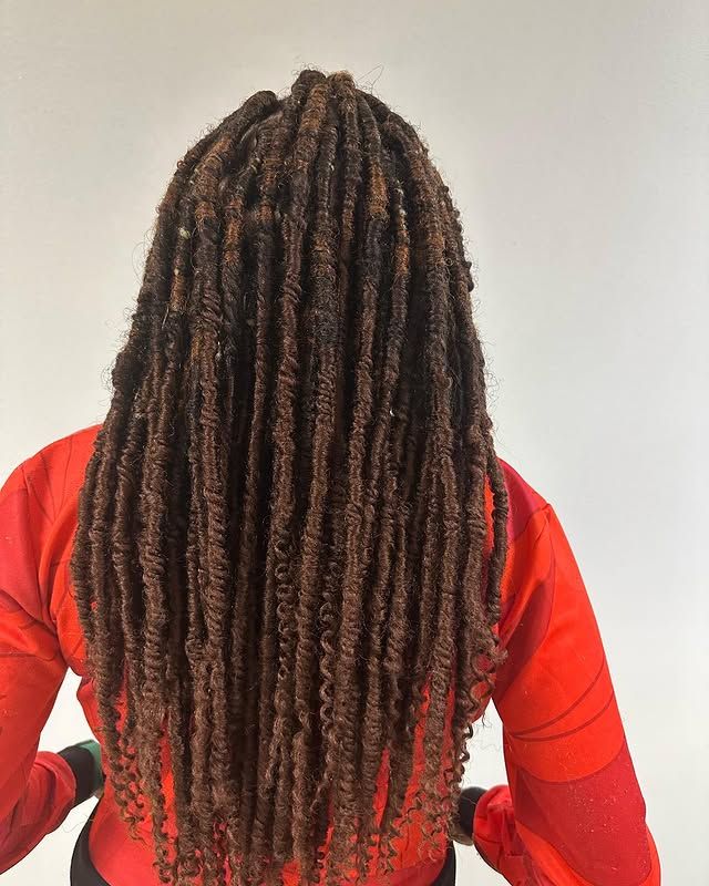 Person with long brown locs wearing a red shirt, shown from behind against a plain light background.