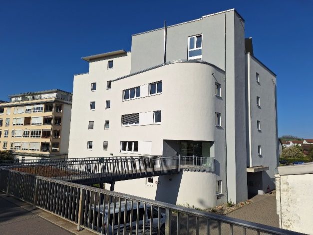 Modernes weißes Apartmentgebäude mit geschwungener Fassade und Metallsteg unter klarem blauen Himmel