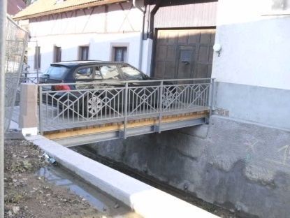 Ein schwarzes Auto parkte neben einer schmalen Brücke mit kunstvollem Geländer neben einem Haus.
