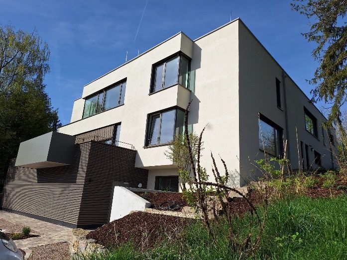 Modernes weißes Apartmentgebäude mit großen Fenstern an einem Hang unter blauem Himmel