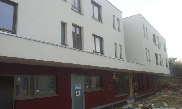 Fassade eines modernen Mehrfamilienhauses mit weißen oberen Stockwerken, roter unterer Fassade und Bauschutt darunter