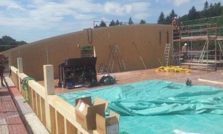 Baustelle mit brauner Wand, Gerüst, mit Plane abgedecktem Boden und einem Gabelstapler unter blauem Himmel