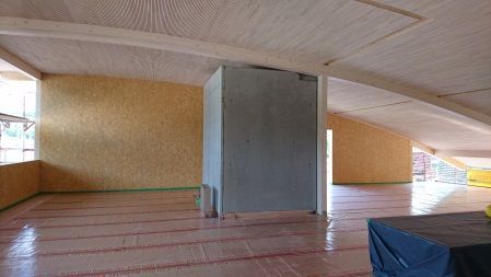 Leerer Innenraum mit niedriger, gewölbter Decke, Holzboden und einer großen grauen Säule in der Mitte.