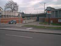 Straßenansicht eines Backsteingebäudes und einer Fußgängerbrücke mit einem geparkten Auto und einem kahlen Baum