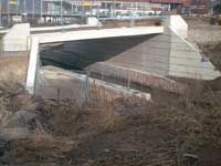 Betonbrücke über einen ausgetrockneten Kanal mit Unkraut und einer darüber verlaufenden Straße