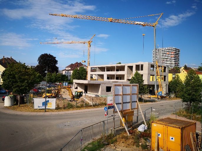 Baustelle mit einem im Bau befindlichen Betongebäude und zwei Turmdrehkranen vor blauem Himmel