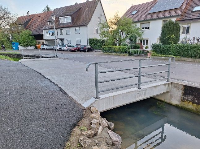 Kleine Brücke über einen Kanal in einer ruhigen Wohnstraße mit Häusern und geparkten Autos.