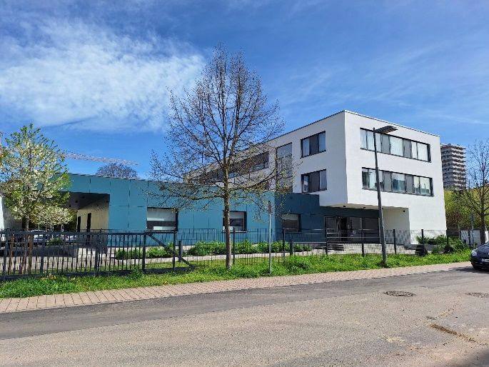 Modernes Schulgebäude mit blau-weißer Fassade hinter einem Zaun an einem sonnigen Tag