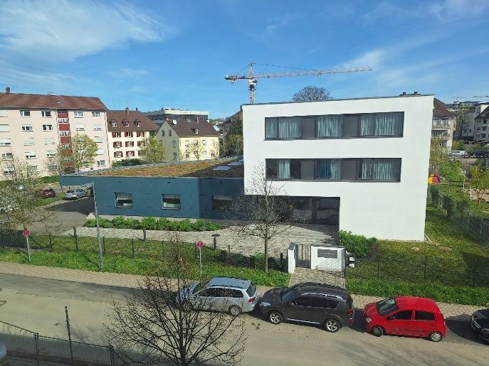 Modernes weißes Wohnhaus mit geparkten Autos auf einer Straße, im Hintergrund ein im Bau befindlicher Kran.