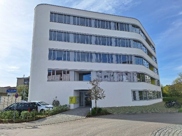 Modernes weißes Bürogebäude mit geschwungenen Balkonen und davor geparkten Autos