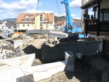 Baustelle mit Bauschutt, einem blauen Kran und einem Arbeiter neben einem dunklen, im Umbau befindlichen Gebäude.