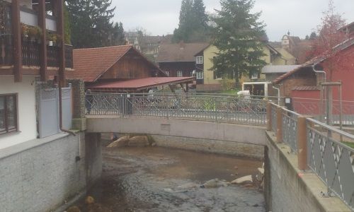 Steinbrücke über einen schmalen Bach zwischen rotgedeckten Häusern an einem bewölkten Tag