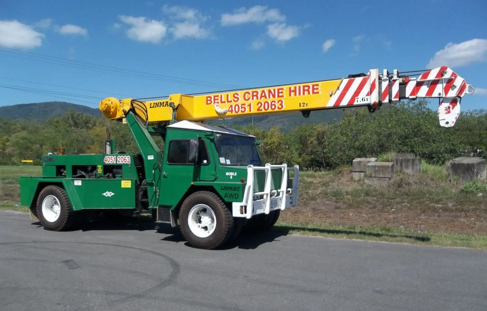 Green crane truck with striped boom parked on a road — Bell's Carrying & Crane Hire Service Pty Ltd in Atherton, QLD