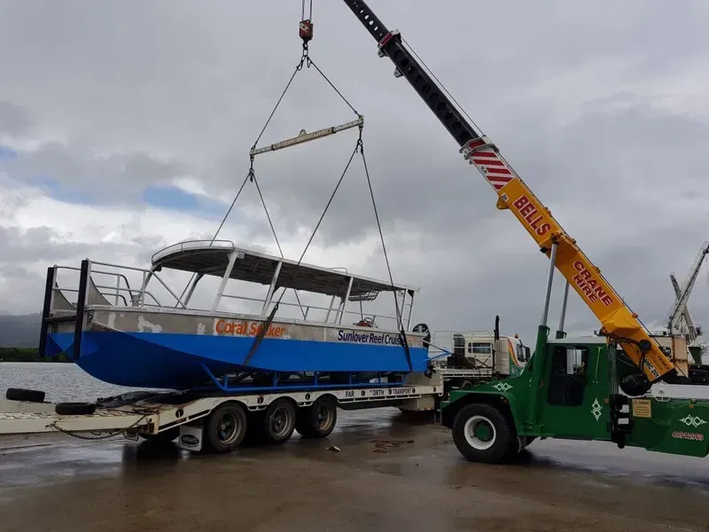 A Crane Lifts a Blue Tour Boat — Bell's Carrying & Crane Hire Service Pty Ltd in Bungalow, QLD