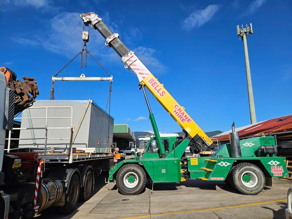 Green crane lifting a large crate onto a flatbed truck — Bell's Carrying & Crane Hire Service Pty Ltd in Atherton, QLD