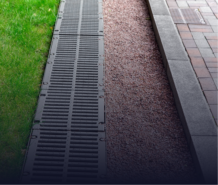 Grassy lawn, gravel bed, and paved sidewalk separated by a dark, slotted drainage channel.