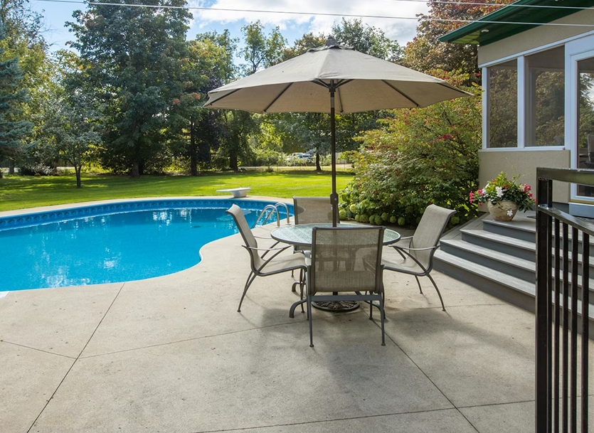 Patio with table, umbrella, chairs, and pool in backyard.