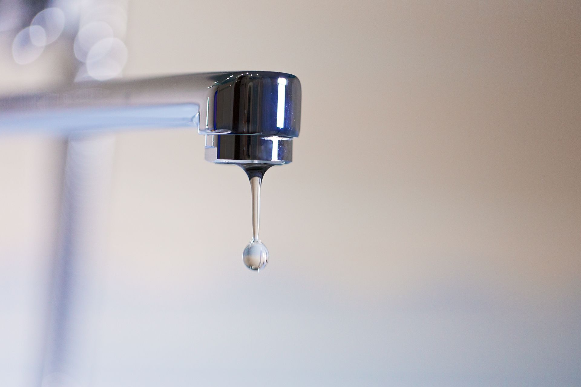 Dripping faucet with a water droplet suspended. Bright chrome against a soft, blurred background.