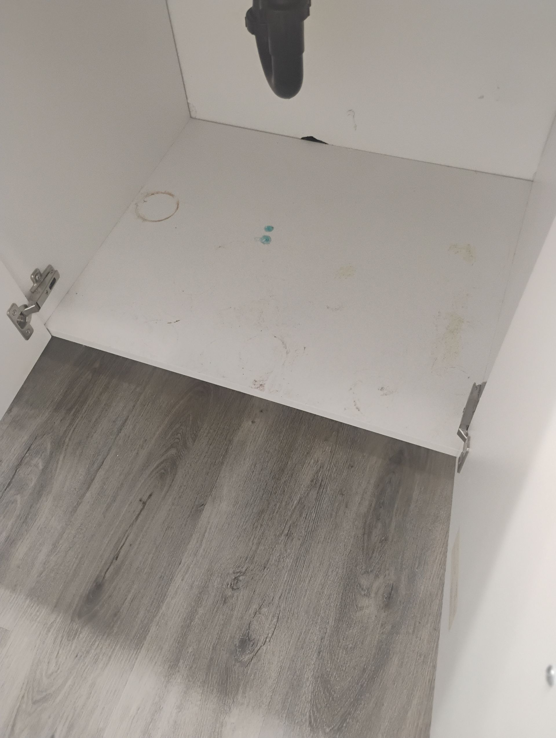 Empty white cabinet interior with a gray wood floor below and visible hinge hardware.