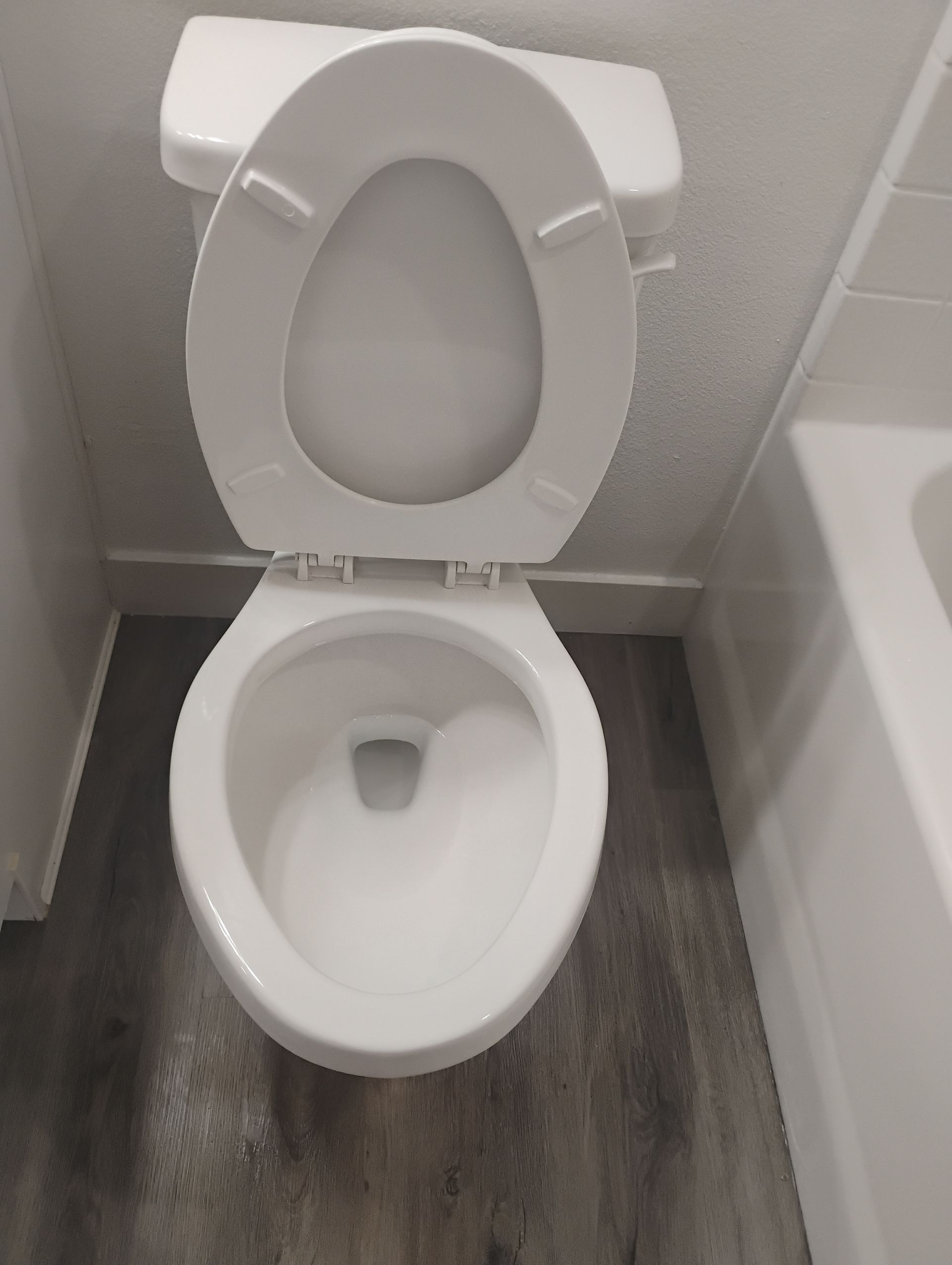 Open toilet in a small bathroom with white tiles and gray flooring.