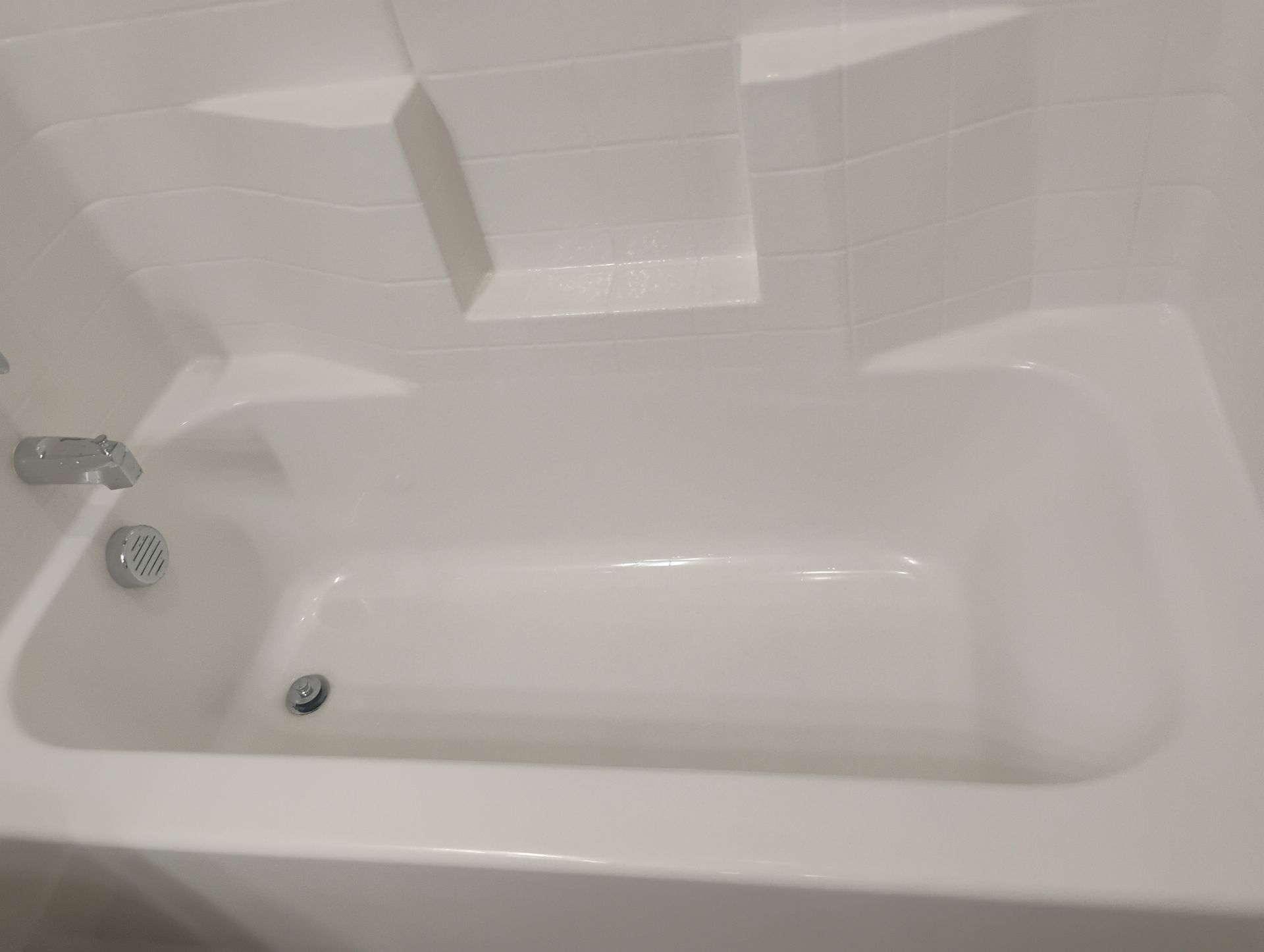 White bathtub with tiled wall, chrome faucet and showerhead, and a grab bar on the left side.