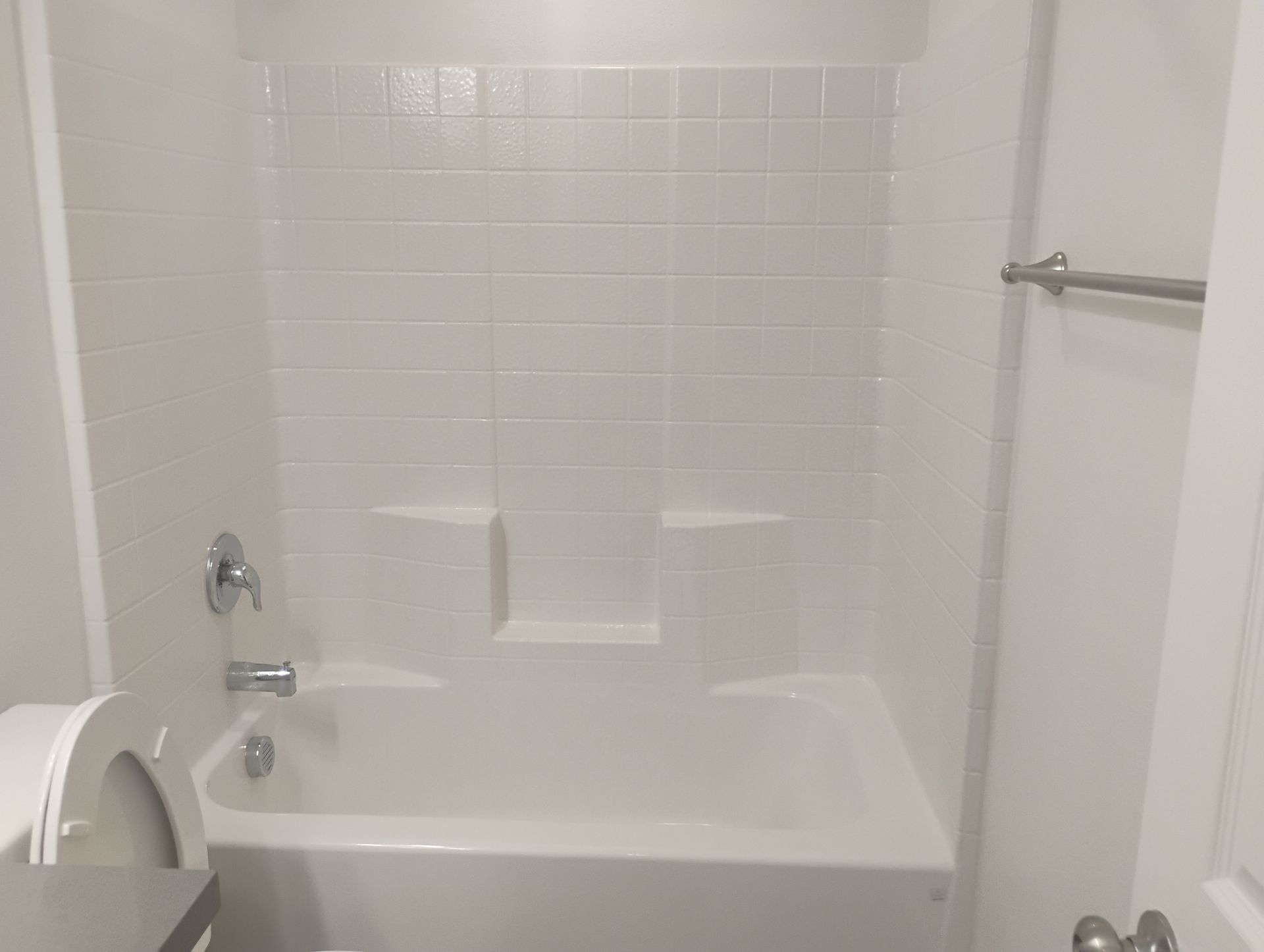White bathroom with a bathtub, tiled shower wall, and towel bar.