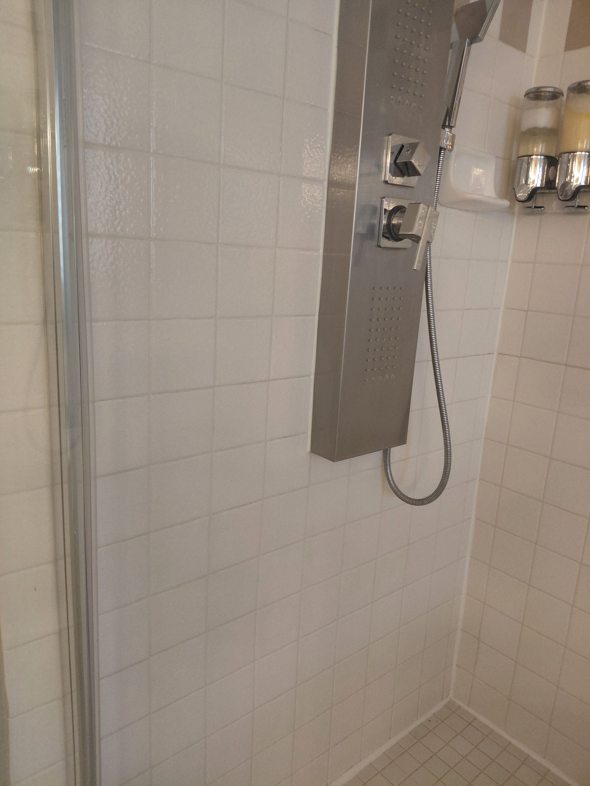 Tiled shower corner with a wall-mounted handheld shower and attached hose