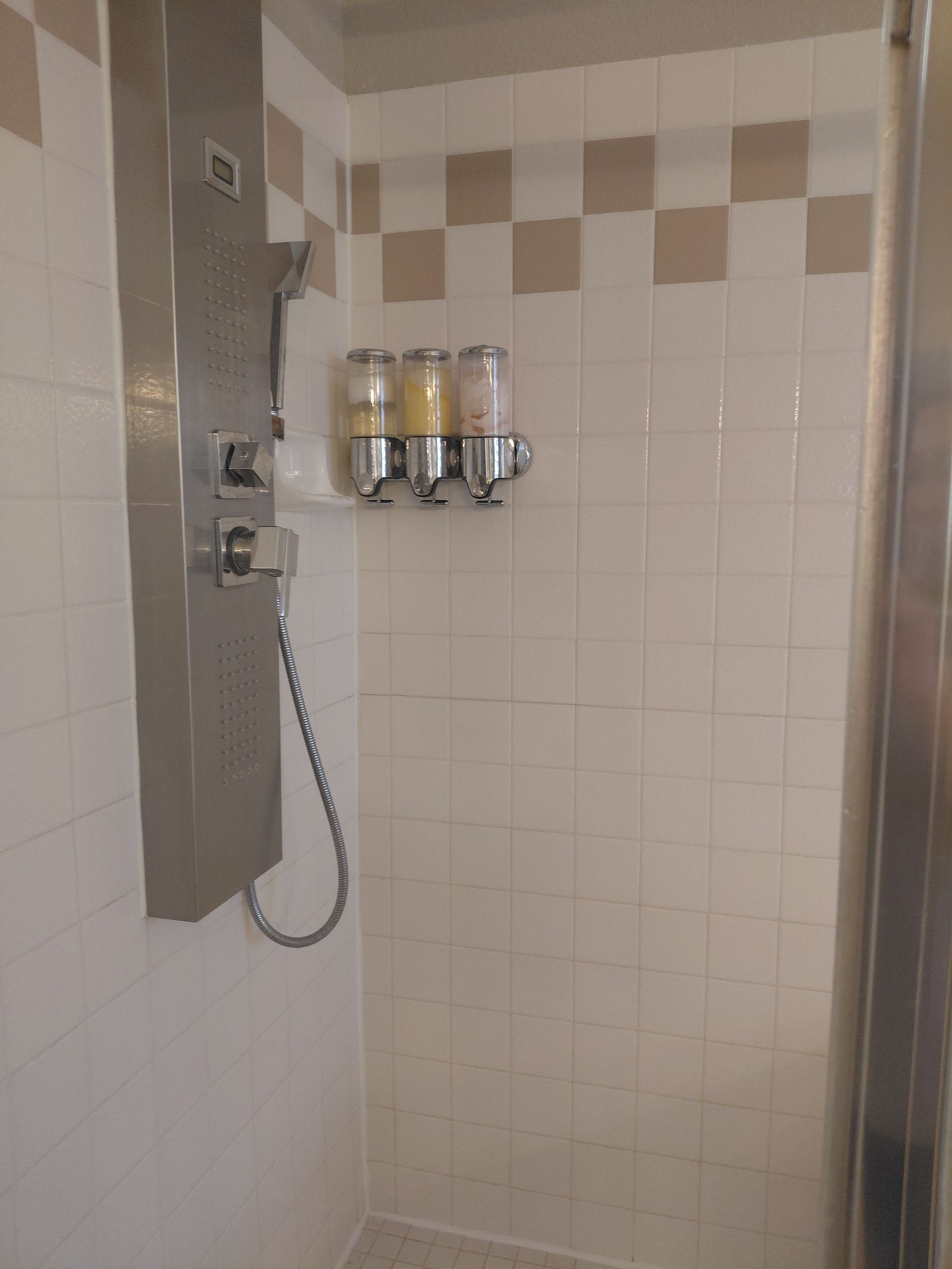 Hotel shower stall with wall-mounted shampoo dispensers and a handheld showerhead