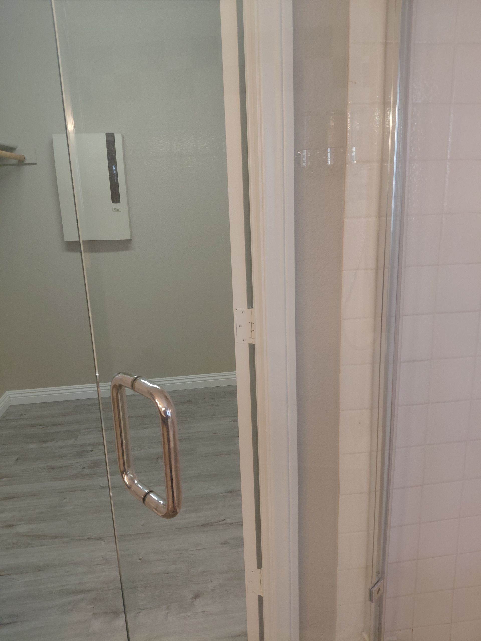 Glass shower door with metal handle in a tiled bathroom stall
