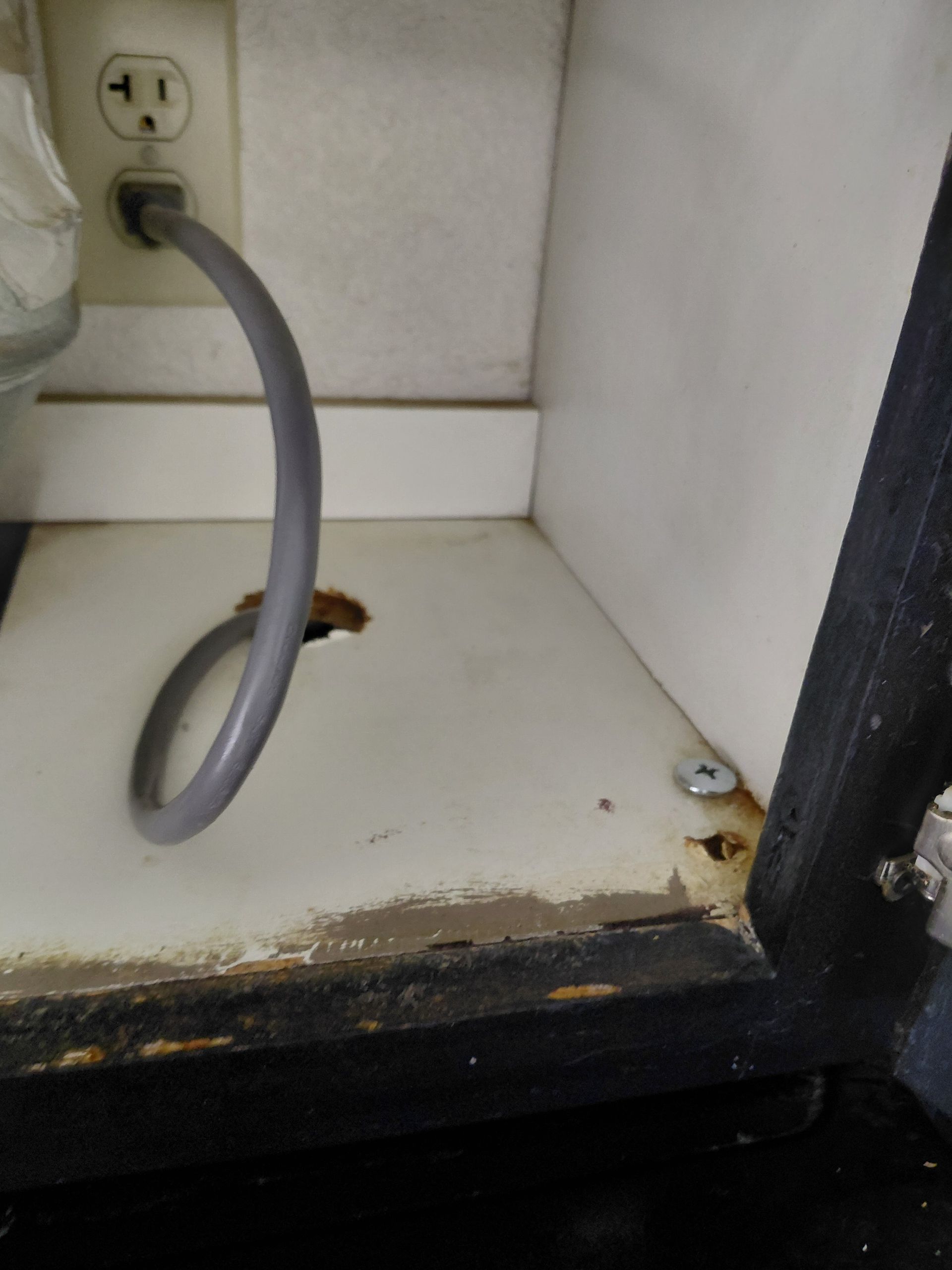 Empty cabinet under a sink with a black drain pipe and white interior, above gray wood flooring
