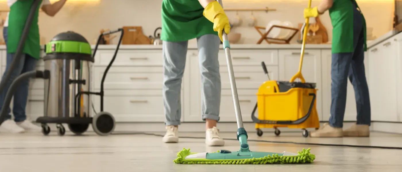 Three cleaners mopping a bright kitchen floor with buckets and supplies