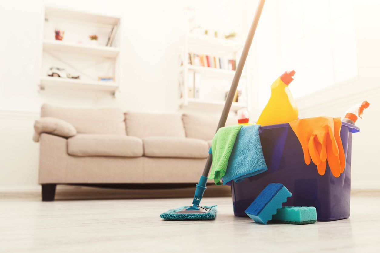 Cleaning supplies with mop and bucket in a bright living room, sofa in the background