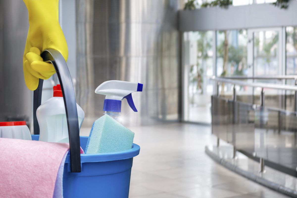 Gloved hand holding cleaning supplies in a blue bucket in a bright lobby