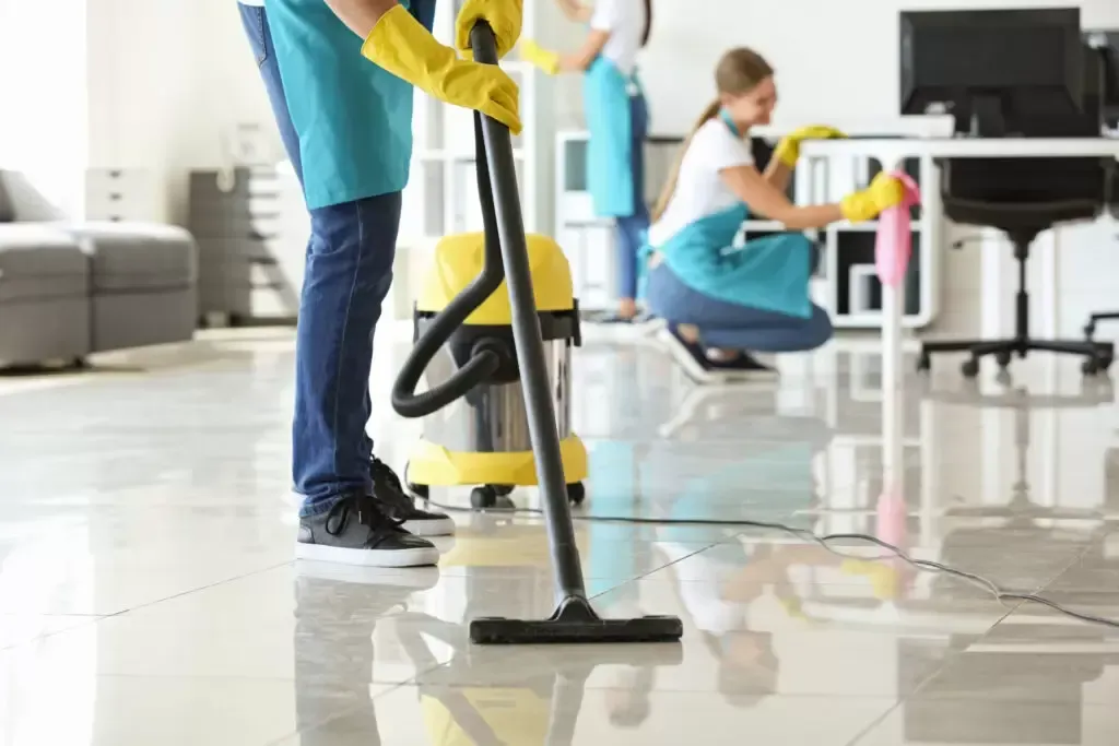 Janitorial workers cleaning a glossy office floor with mops and a vacuum in a bright workspace