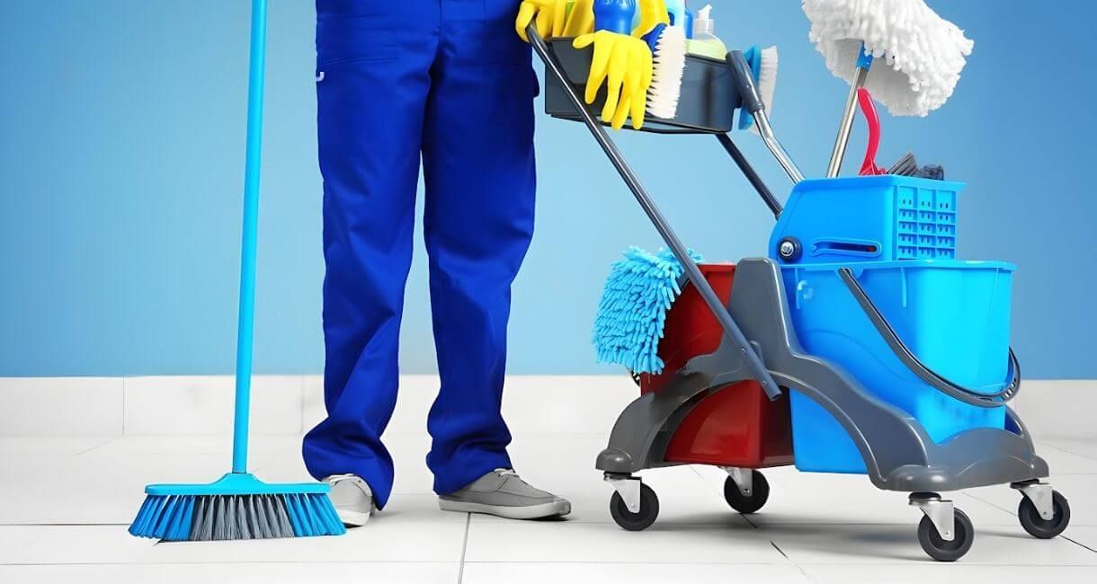 Janitor in blue pants cleaning floor with mop and cart of supplies