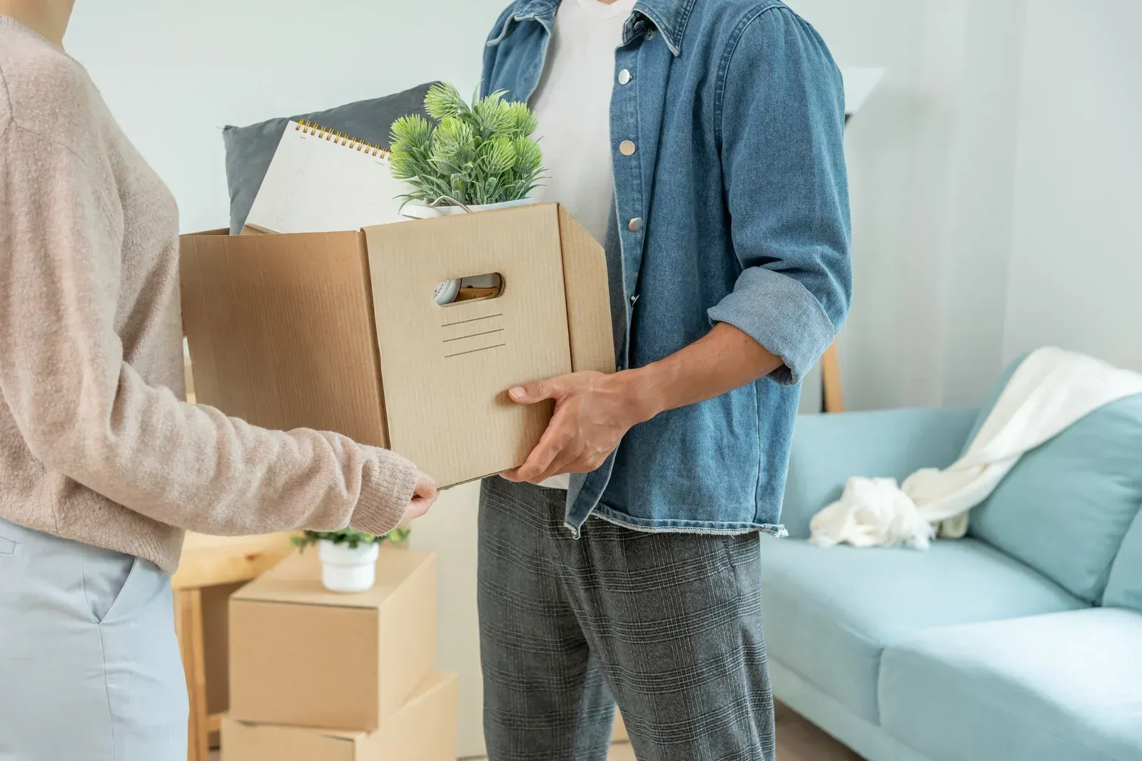 Two people exchanging a cardboard box in a bright living room with a blue sofa