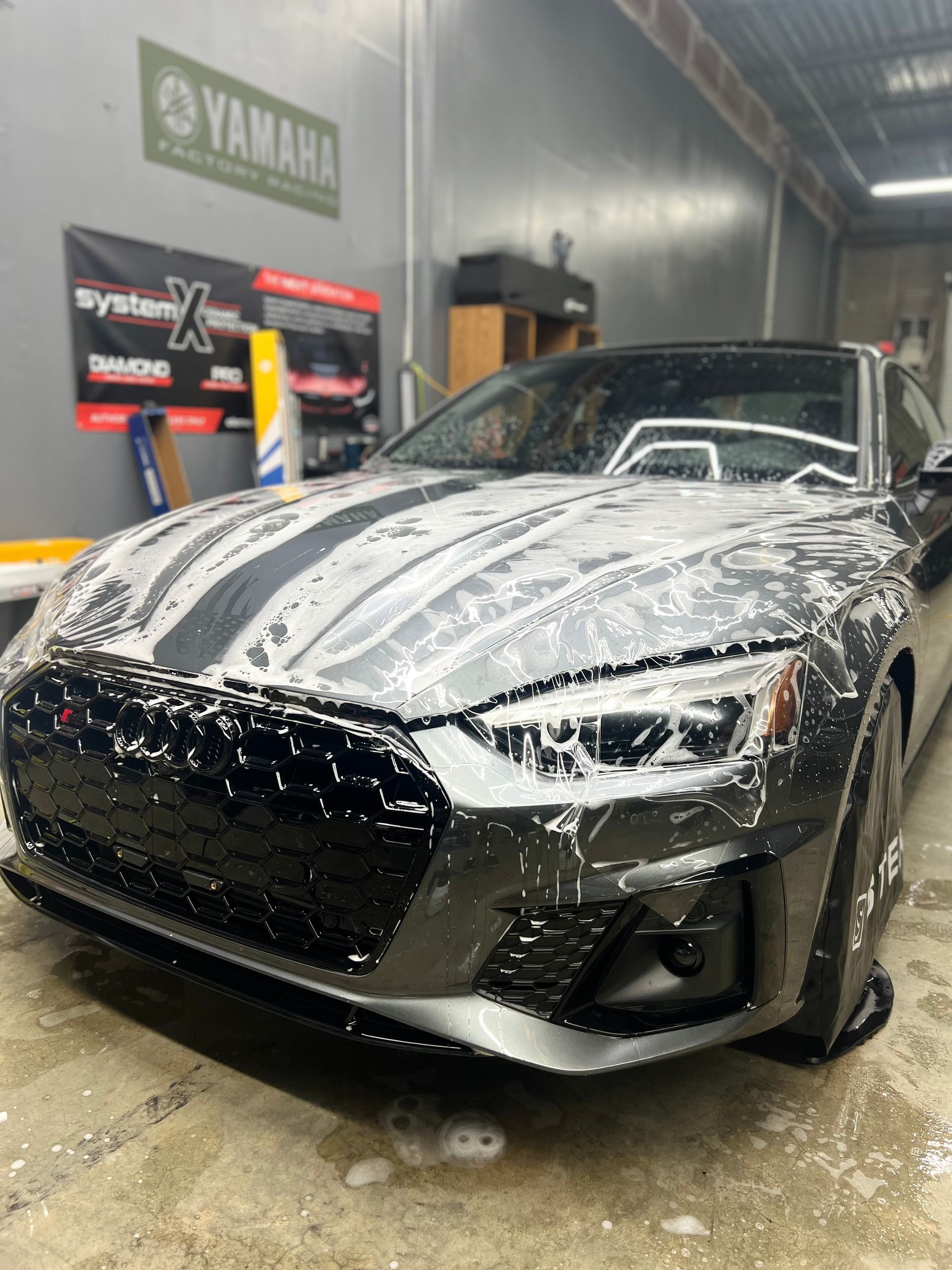 Black sports car covered in foam at a car wash, with soap dripping on the floor