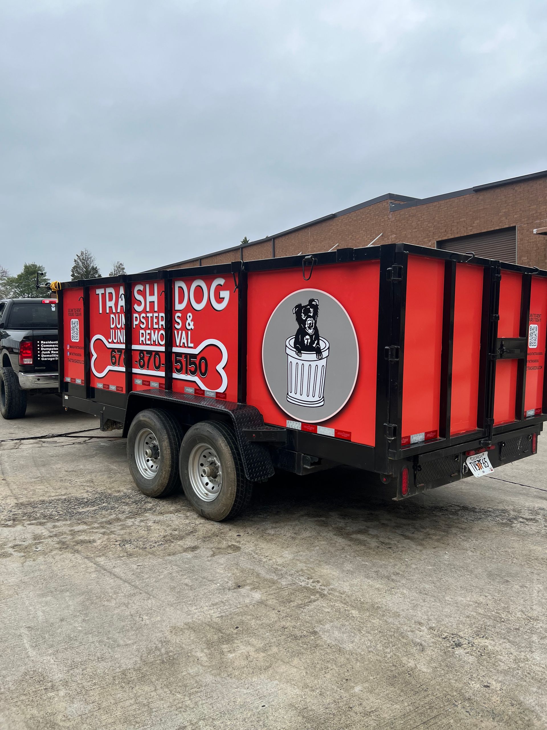 Red fish-and-dog trailer with bold white lettering, parked beside a building on a gravel lot.