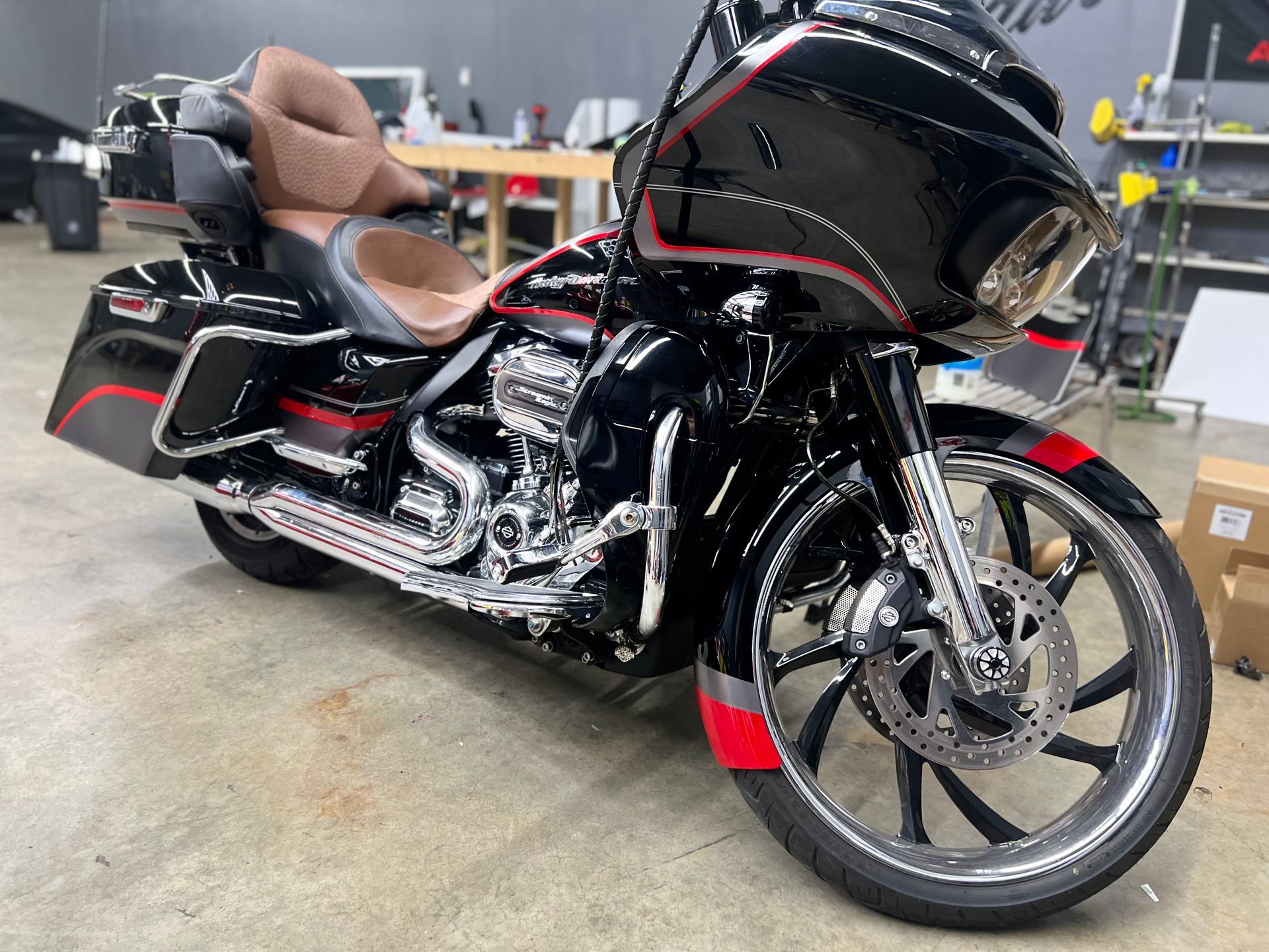 Black custom touring motorcycle with red accents parked indoors on a workshop floor.