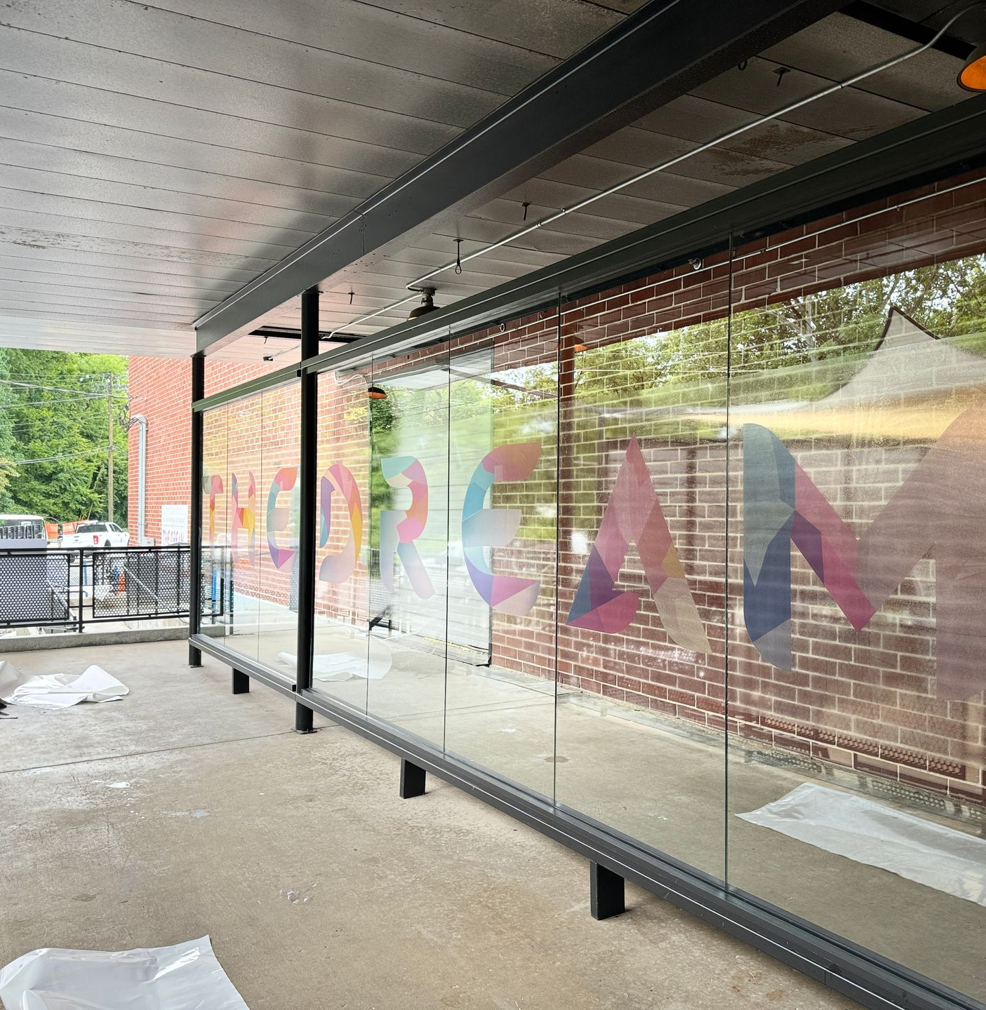 Covered walkway with colorful mural on glass wall and a brick building outside