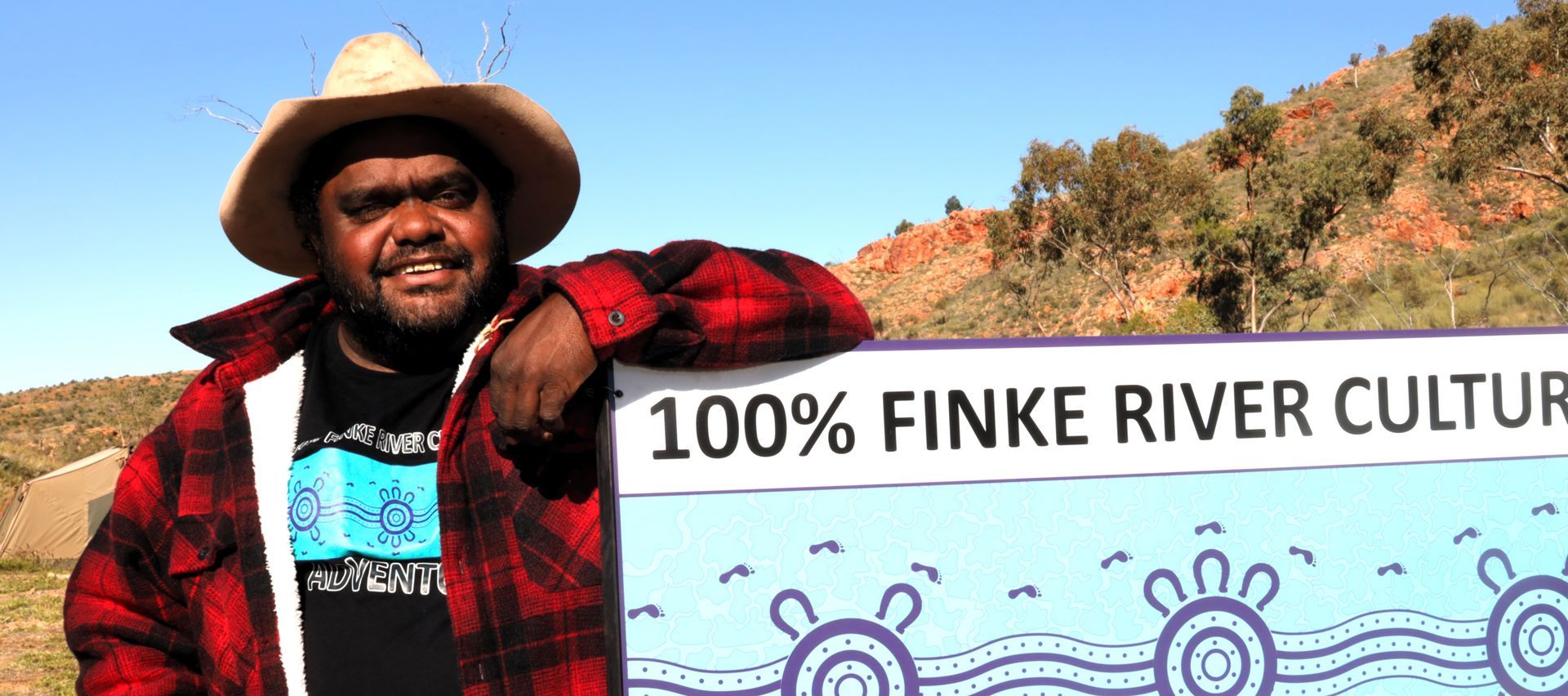 A man standing next to a sign that says 100 % finke river culture