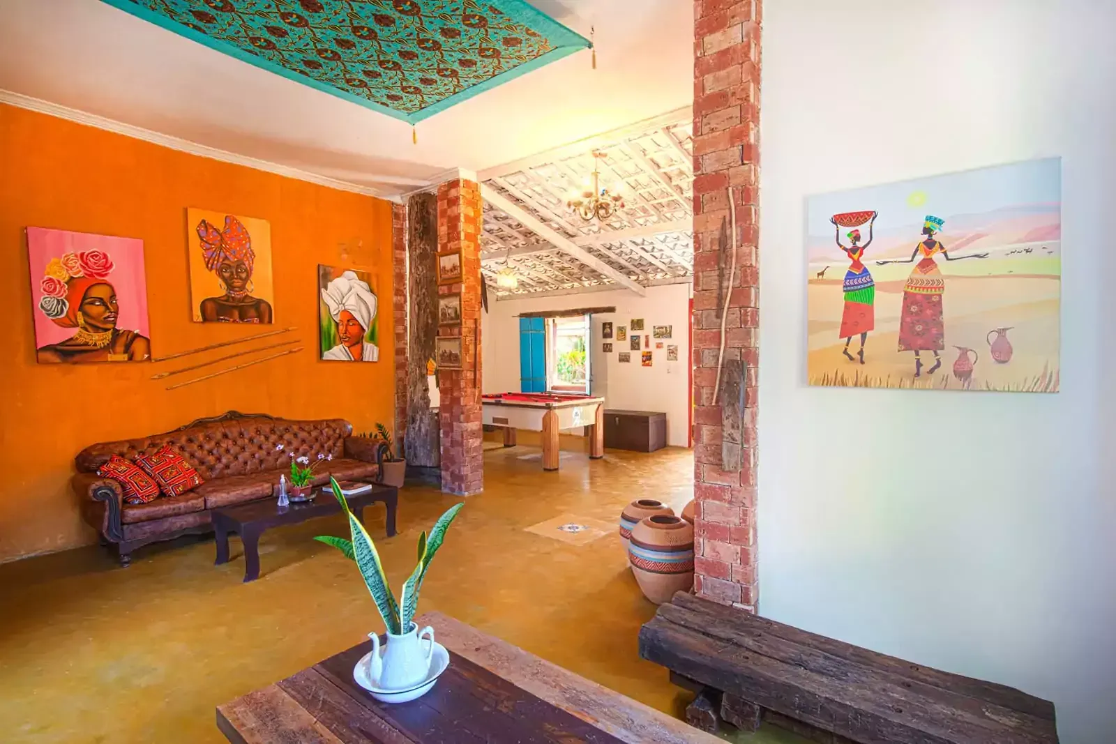 Uma sala de estar com um sofá, mesa e pinturas na parede.- Hostel-Mama-Africa-2