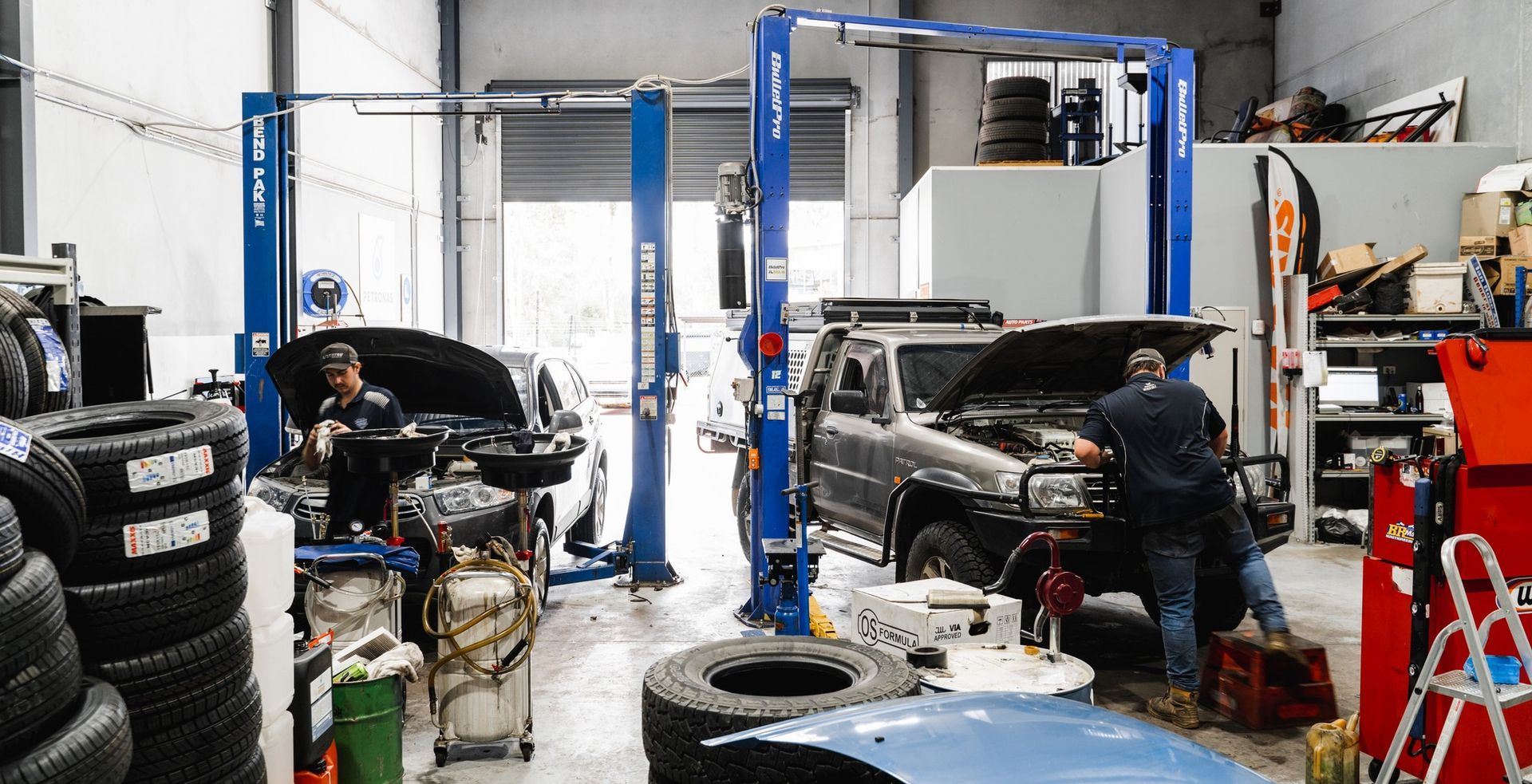 Auto repair shop with a mechanic working on a black car near stacks of tires and tools  — Gardiner Automotive & Performance in Rutherford, NSW