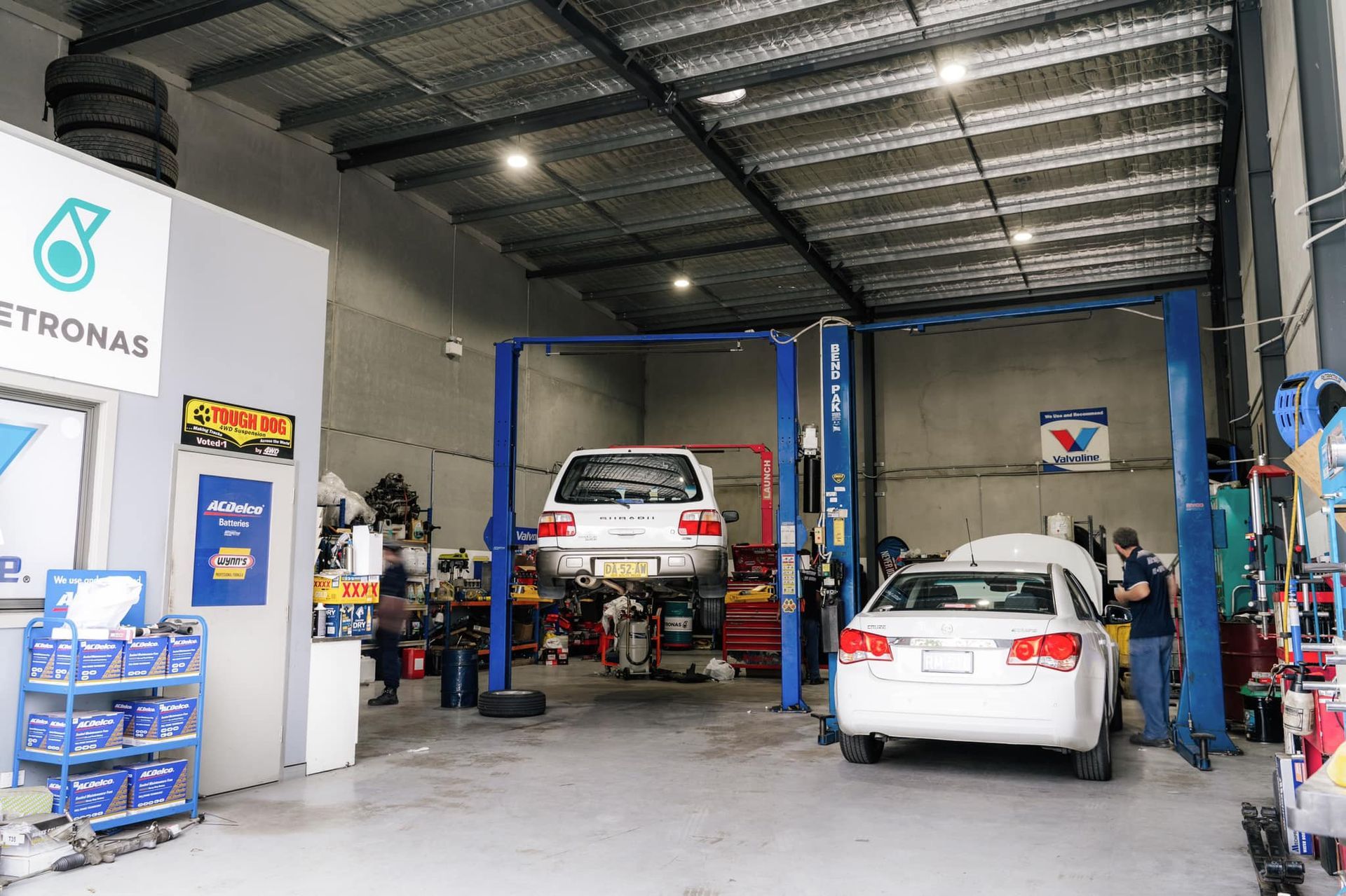 Auto repair shop with two white cars on lifts and blue service equipment inside a garage — Gardiner Automotive & Performance in Rutherford, NSW
