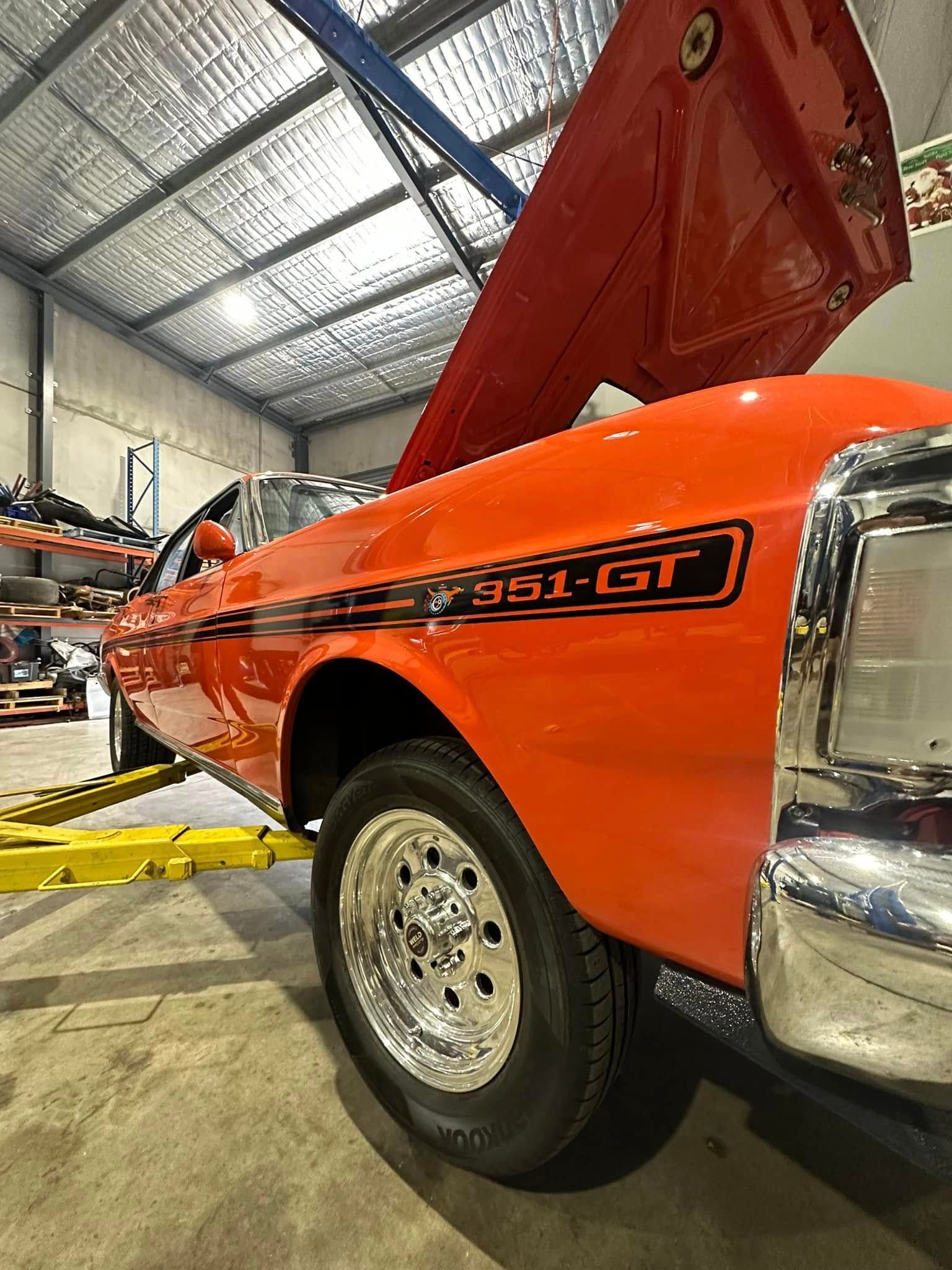 Orange classic car on a lift inside a garage, showing its front side and chrome wheel — Gardiner Automotive & Performance in Rutherford, NSW