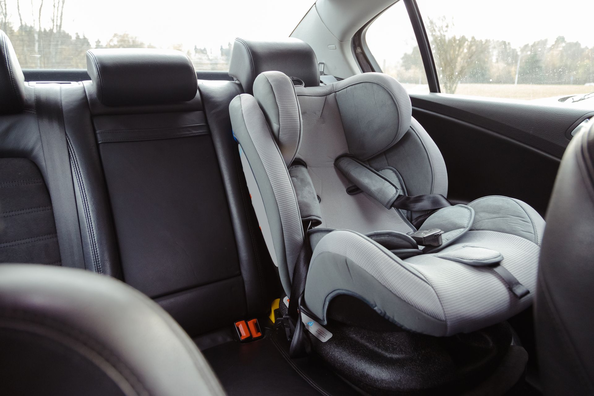 Gray child car seat secured on a black car back seat, facing sideways in the rear passenger area.