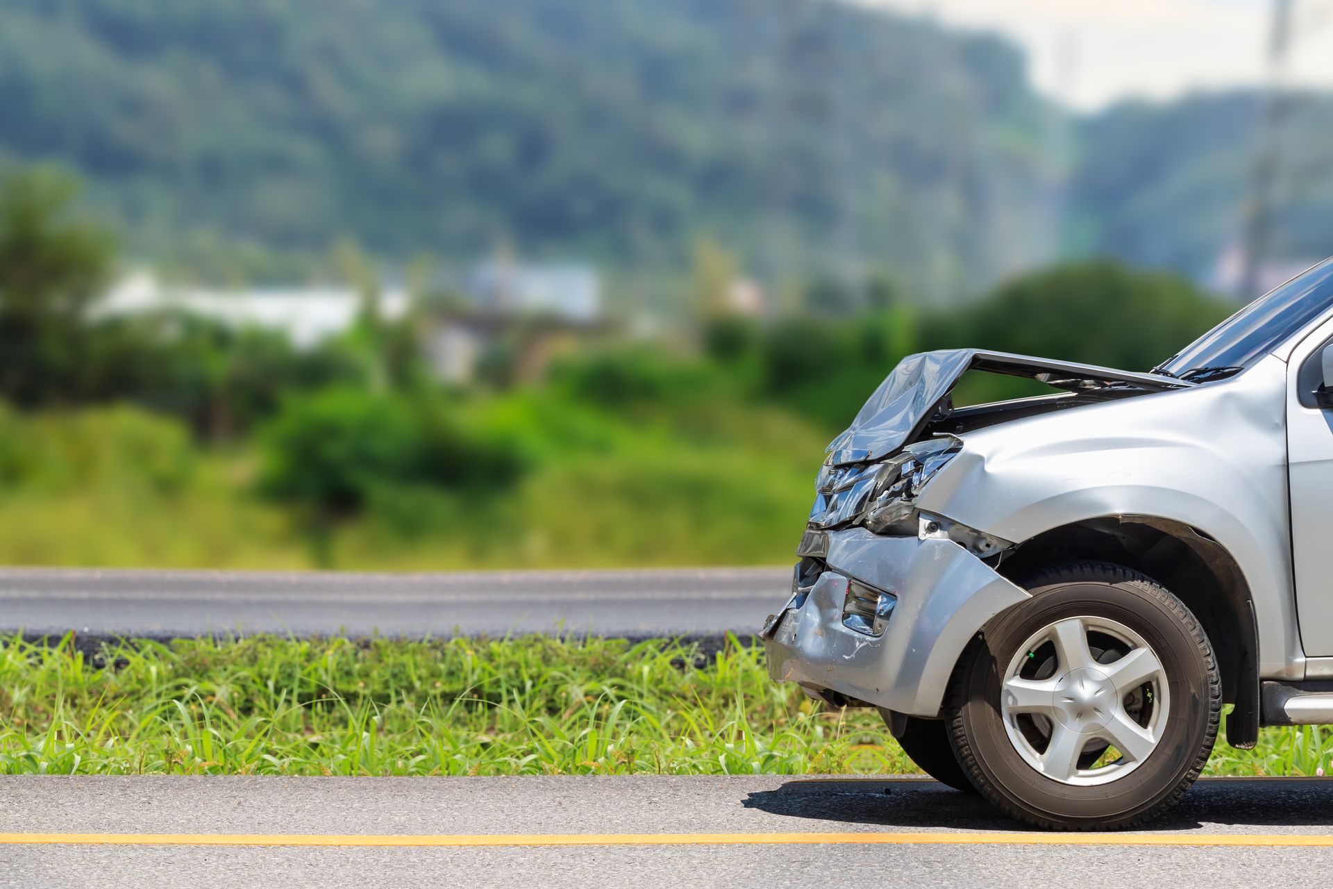 Damaged silver car with crumpled front end on roadside after a crash