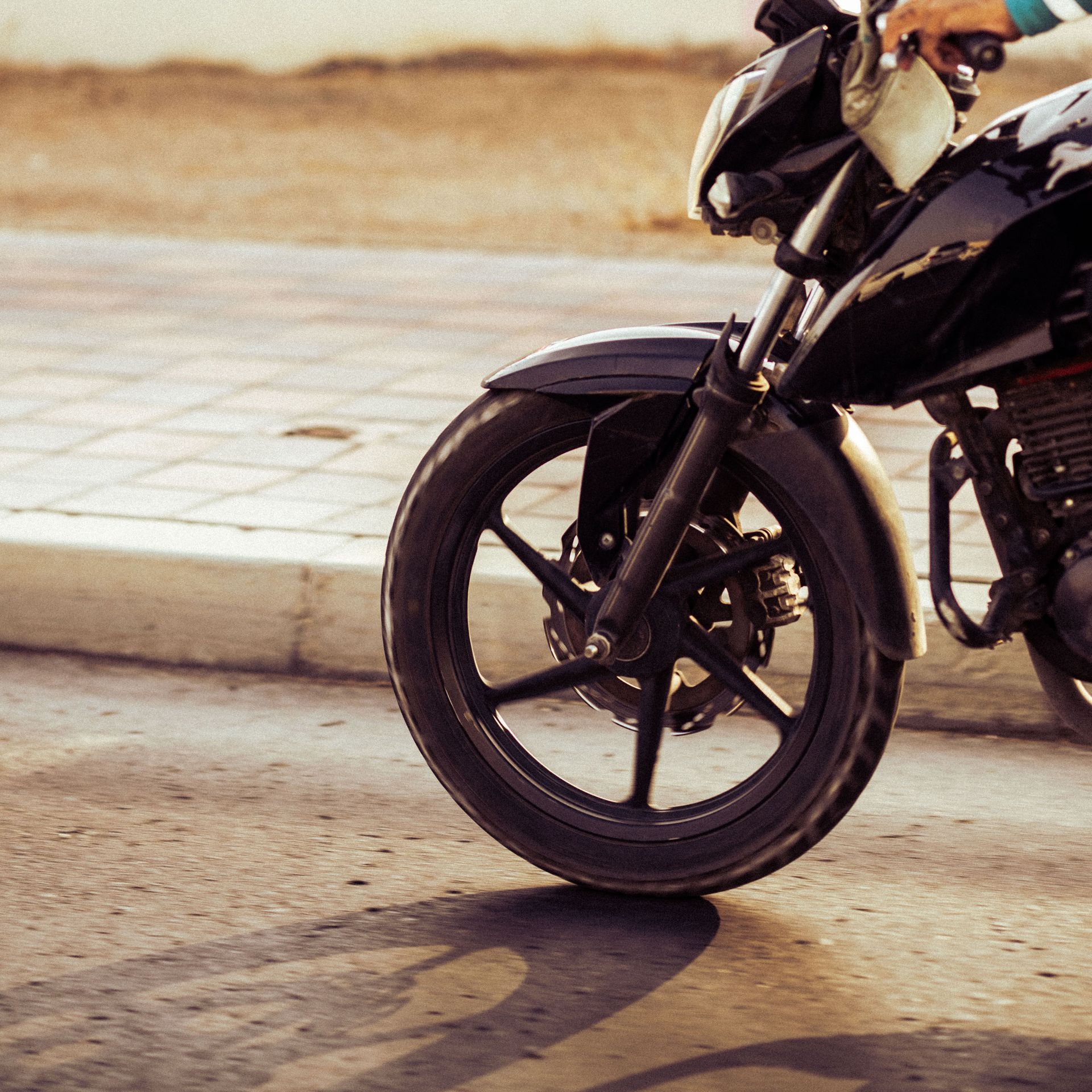 Front wheel of a black motorcycle parked on a sunlit paved street